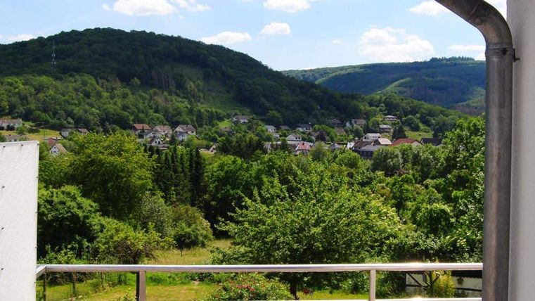 Eine malerische Aussicht auf grüne Hügel und ein kleines Dorf. Der Himmel ist blau mit einigen weißen Wolken.