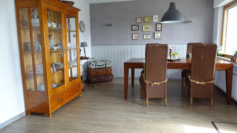 Ein gemütlicher Essbereich mit einem Holzschrank und einem großen Tisch. Die Einrichtung ist hell und freundlich, mit Bilderrahmen an der Wand.