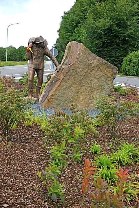 Eine Statue eines Tauchers, der mit einem großen Stein interagiert. Umgeben von bunten Pflanzenanlagen.