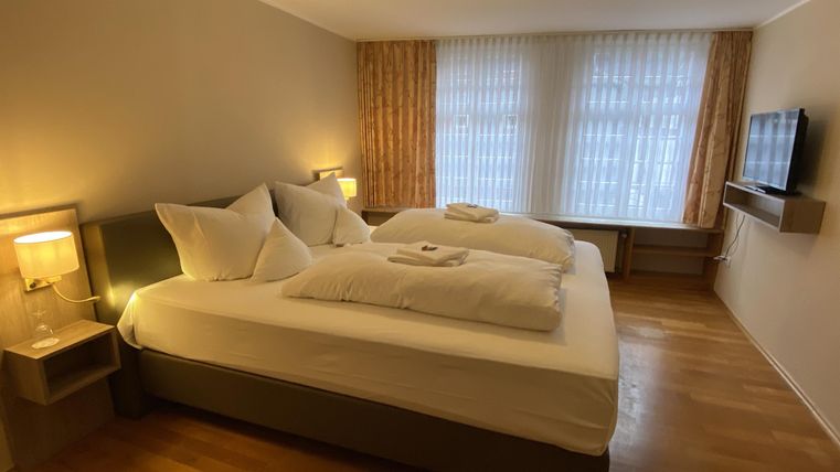 Ein helles Hotelzimmer mit zwei Betten und großen Fenstern. Es gibt moderne Möbel und sanfte Beleuchtung.