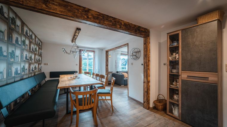 Ein modernes Esszimmer mit einem großen Holztisch und Holzstühlen. An der Wand sind Fotos ausgestellt, und ein Kühlschrank steht in der Ecke.