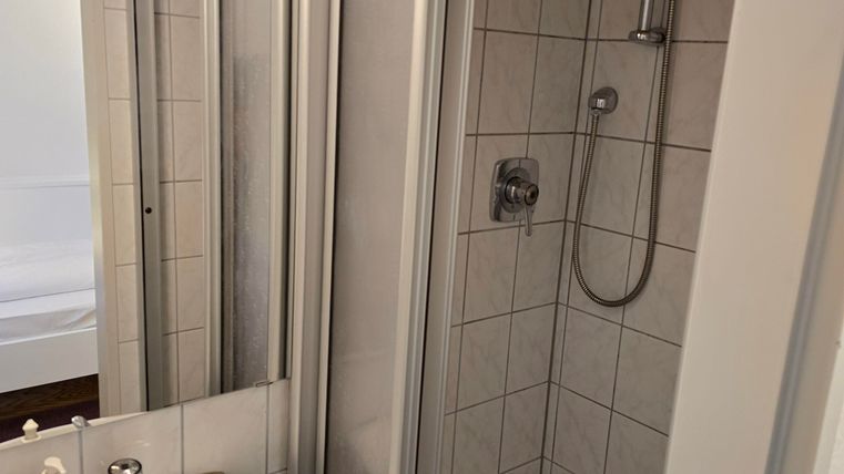 Ein modernes Badezimmer mit einer Dusche und einem Waschbecken. Die Wände sind gefliest und es gibt einen Spiegel.