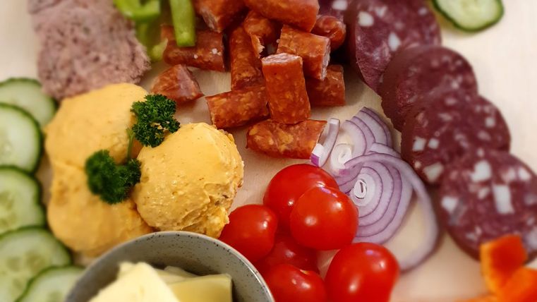Ein bunter Teller mit verschiedenen Wurst- und Käseaufschnitten, frischem Gemüse und Dip. Die Zutaten sind schön angerichtet und laden zum Genießen ein.