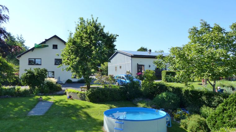 Ein schöner Garten mit einem blauen Pool und viel Grün. Im Hintergrund sind zwei Häuser und Bäume zu sehen.