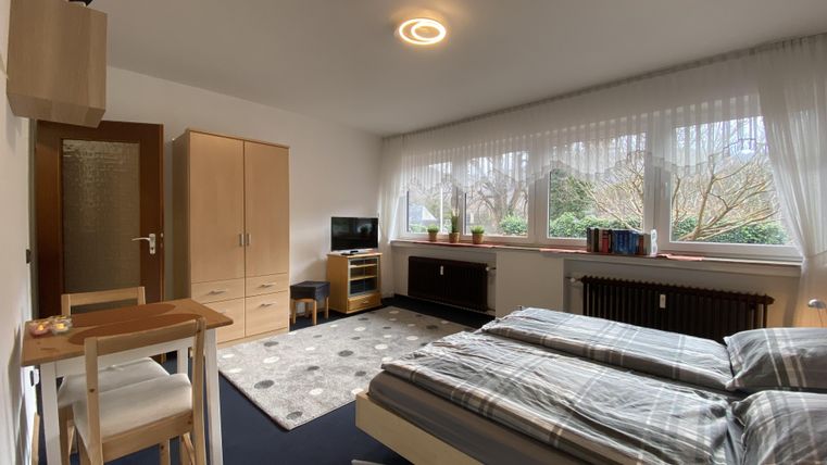 Ein gemütliches Schlafzimmer mit zwei Betten und einem Schreibtisch. Große Fenster lassen viel Tageslicht herein.