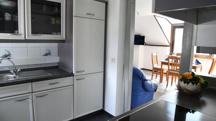 Eine moderne Küche mit weißen Schränken und Edelstahlgeräten. Im Hintergrund befindet sich ein gemütlicher Wohnbereich mit einem Tisch und Stühlen.