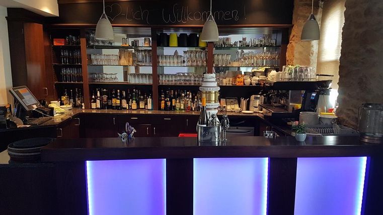 Eine stilvolle Bar mit beleuchtetem Tresen und einer Vielzahl von Getränken im Hintergrund. Die Einrichtung wirkt modern und einladend.