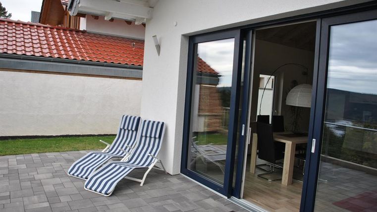 Eine sonnige Terrasse mit zwei Liegestühlen und Blick auf das Wohnzimmer. Die Umgebung ist ruhig und einladend.