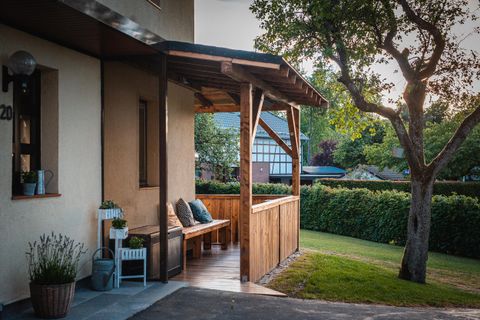 Ein gemütlicher Außenbereich mit einer Holzveranda und einer Bank. Im Hintergrund sind ein gepflegter Garten und einige Bäume zu sehen.