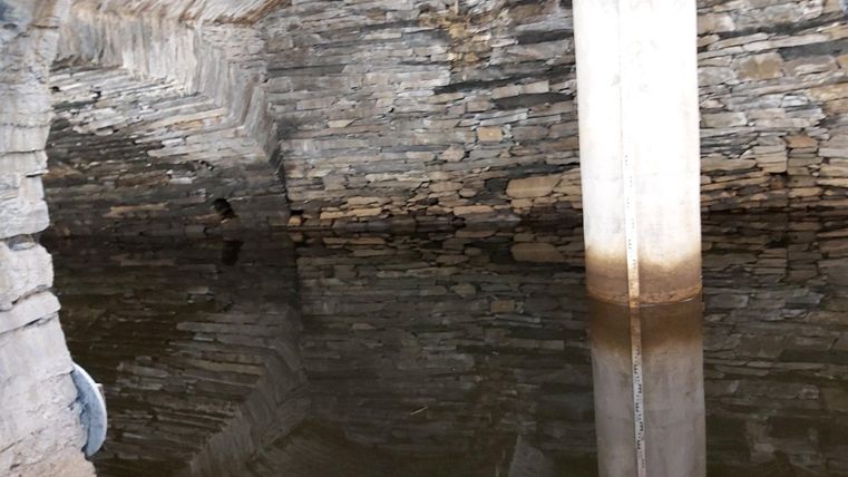 Ein unterirdischer Raum mit steinernen Wänden und Wasseroberfläche. Ein Säulenständer steht in der Mitte und reflektiert sich im Wasser.