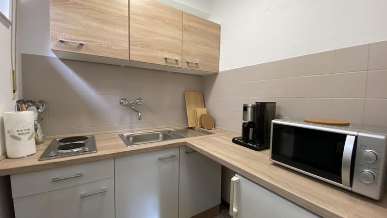Eine moderne Küche mit hellen Holzschränken und einer praktischen Anordnung. Sie enthält einen Herd, einen Wasserhahn, eine Kaffeemaschine und eine Mikrowelle.