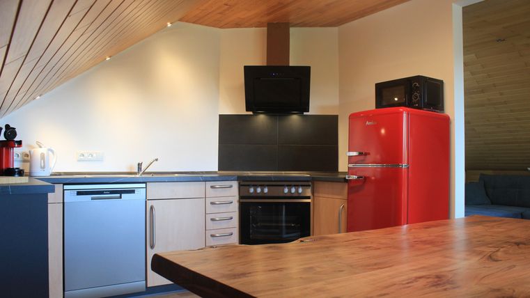 Eine moderne Küche mit Holzdecke und Geräten in eleganten Farben. Der rote Kühlschrank ist ein auffälliger Blickfang.