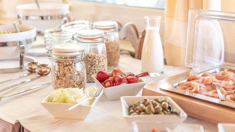 Ein leckerer Frühstückstisch mit verschiedenen Lebensmittelangeboten. Es gibt Müsli, frisches Obst und Milch in Glaskaraffen.