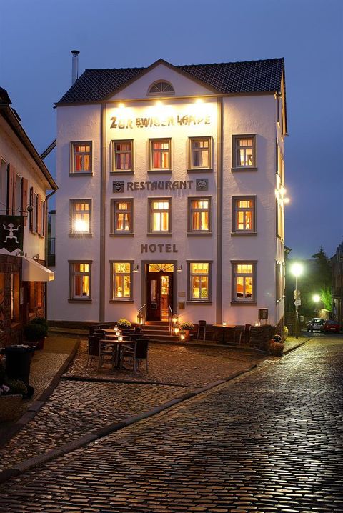 Ein charmantes Hotel mit einem Restaurant an einer ruhigen Straße. Das Gebäude ist hell erleuchtet und hat einen gemütlichen, einladenden Eindruck.
