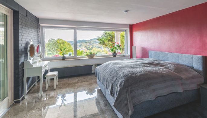 Ein modernes Schlafzimmer mit einem großen Bett und Fenster mit Blick auf die Landschaft. Die Wände sind in sanften Farben gestrichen, und es gibt einen eleganten Schminktisch.