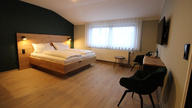 Ein modernes Schlafzimmer mit einem großen Bett und stilvollen Möbeln. Die Fenster lassen viel Tageslicht herein und schaffen eine angenehme Atmosphäre.