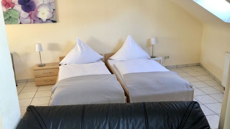 Ein gemütliches Schlafzimmer mit zwei Einzelbetten und einem schwarzen Sofa. Die Wände sind hell und es gibt eine Blumentapete.