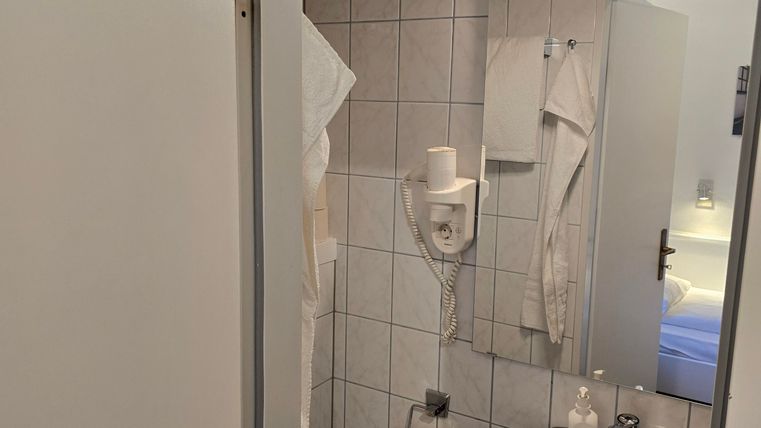 Ein kleines Badezimmer mit Toilette, Waschbecken und Spiegel. Weiße Fliesen und Handtücher sind sichtbar.