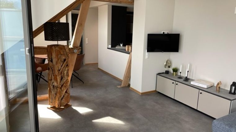 Ein modernes Wohnzimmer mit Holzdetails und einem offenen Raumkonzept. Die Einrichtung ist schlicht und funktional, mit einem Fernseher und einem gemütlichen Sessel.
