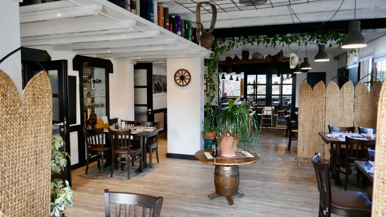 Ein gemütliches Restaurant mit Holzmöbeln und Pflanzen. Der Raum ist hell und einladend, mit einer warmen Atmosphäre.