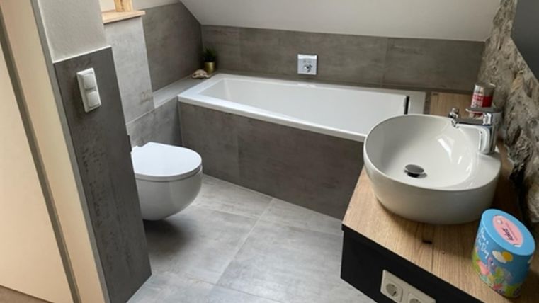 Ein modernes Badezimmer mit einer Badewanne, einer Toilette und einem Waschbecken. Die Wände sind in neutralen Farben gehalten, und es gibt ein Dachfenster für natürliches Licht.