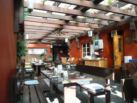 Ein einladender Außenbereich eines Restaurants mit Holzmöbeln und begrünten Wänden. Die Sonneneinstrahlung sorgt für eine freundliche Atmosphäre.