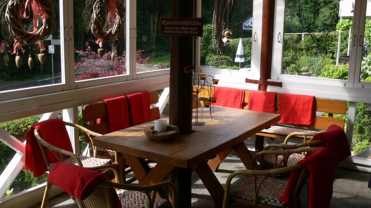 Ein gemütlicher Essbereich mit einem Holztisch und Stühlen, dekoriert mit roten Decken. Große Fenster bieten einen Blick auf die grüne Umgebung.