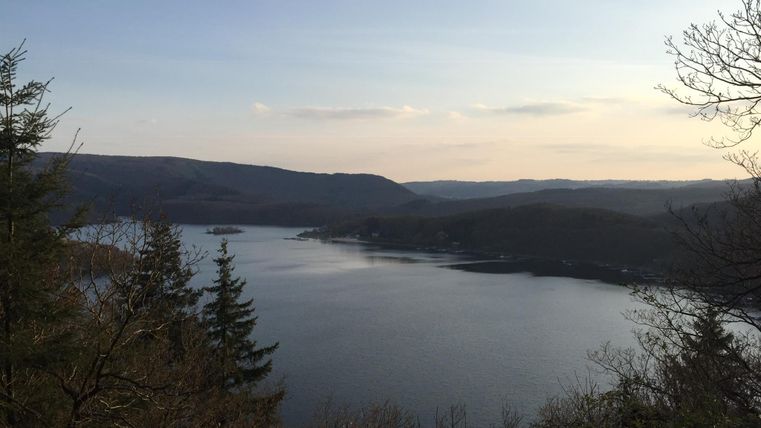 Eine ruhige Landschaft mit einem großen See und sanften Hügeln im Hintergrund. Der Himmel ist klar und es ist Abendlicht zu sehen.