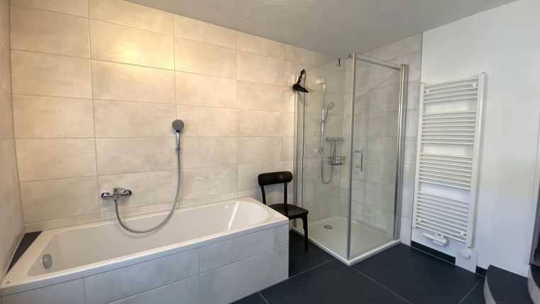 Ein modernes Badezimmer mit einer Badewanne und einer separaten Dusche. Die Wände sind hell gefliest und es gibt einen Handtuchheizkörper.