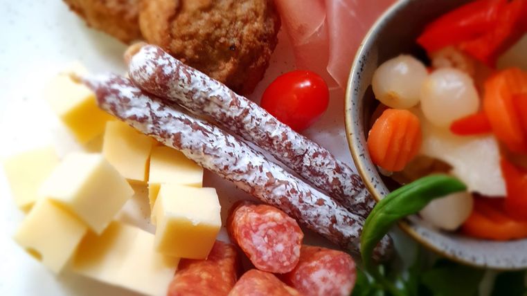 Ein Teller mit verschiedenen Köstlichkeiten, darunter Wurst, Käse, Schinken und Gemüse. Die Anrichtung ist ansprechend und farbenfroh.