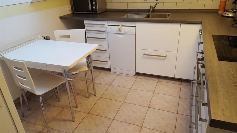 Eine moderne Küche mit weißen Schränken und einer kleinen Sitzecke. Der Boden ist gefliest und die Arbeitsplatte ist aus Holz.