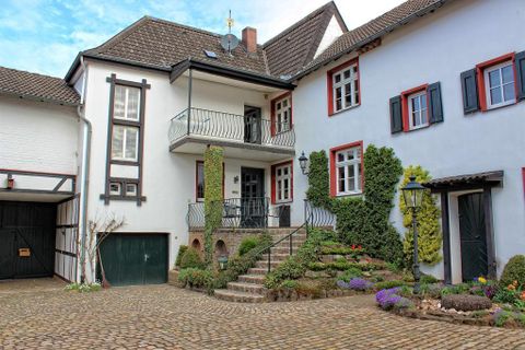 Ein charmantes Haus mit einem Balkon und grünen Pflanzen. Der Innenhof ist mit Blumen und einem Steinweg gestaltet.