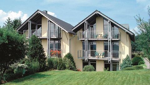 Zwei moderne Häuser mit Balkonen in einem grünen Garten. Umgeben von Bäumen und Sträuchern, strahlen sie eine ruhige Wohnatmosphäre aus.