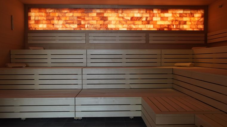 Ein entspannender Saunabereich mit Holzliegen und sanftem Licht. Die Wände sind mit himmelsalzfarbenen Steinen dekoriert.