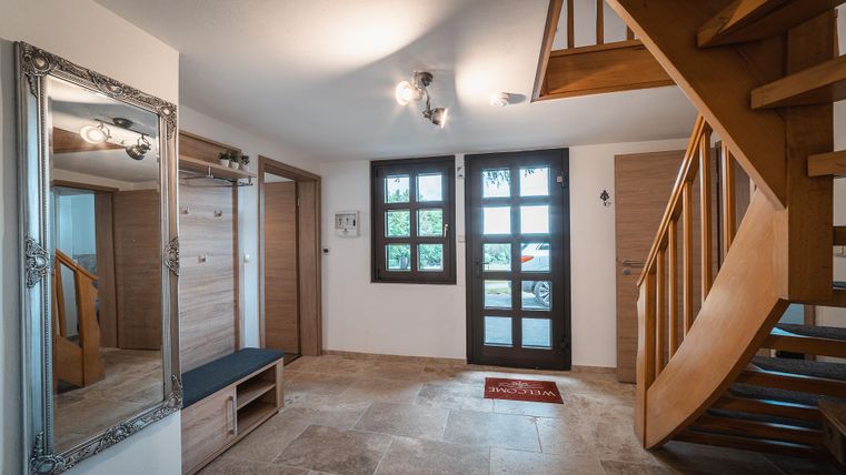 Ein heller Eingangsbereich mit einer Holztreppe und einem großen Spiegel. Die Wände sind neutral, und ein Teppich lädt zum Betreten ein.