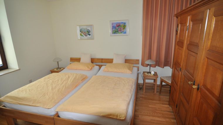 Ein gemütliches Schlafzimmer mit zwei Einzelbetten und Holzfußboden. Die Wände sind hell gestrichen und es gibt einige Bilder sowie Vorhänge.