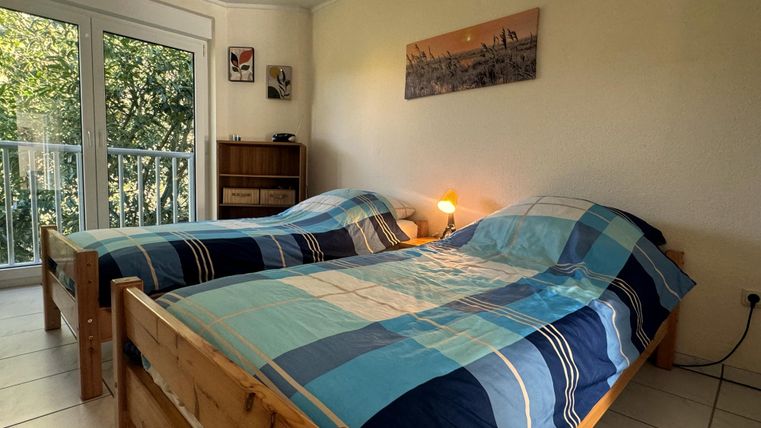 Ein gemütliches Zimmer mit zwei Einzelbetten und bunten Bettdecken. Große Fenster sorgen für viel Tageslicht und einen Blick ins Grüne.