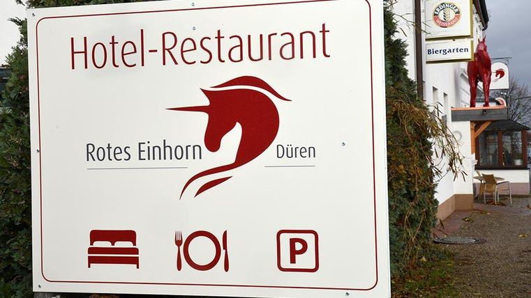 Ein Schild für das Hotel-Restaurant "Rotes Einhorn" in Düren. Es zeigt Symbole für Übernachtung, Essen und Parkplätze.