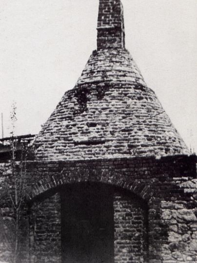 Ein historisches, gemauertes Gebäude mit einem konischen Dach. Die Struktur zeigt Abnutzungserscheinungen und ist umgeben von einer alten Mauer.