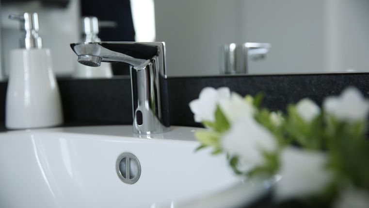 Ein modernes Waschbecken mit einem glänzenden Wasserhahn. Neben dem Waschbecken steht eine weiße Blumenvase.