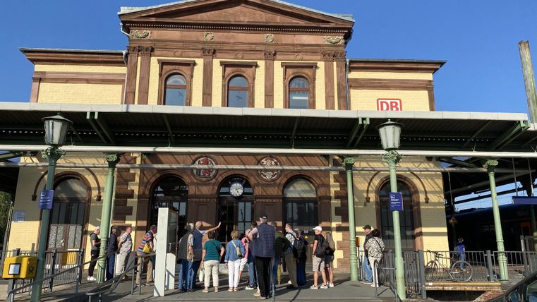 Ein historischer Bahnhof mit einer markanten Fassade. Vor dem Gebäude sind zahlreiche Menschen versammelt.