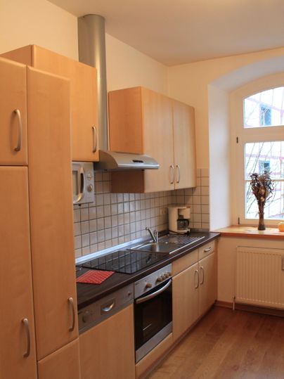 Eine moderne Küche mit Holzschränken und einem Herd. Sie hat ein Fenster mit Blick nach draußen und eine gemütliche Atmosphäre.