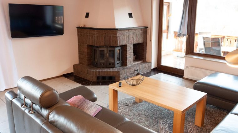 Ein modernes Wohnzimmer mit einem gemütlichen Kamin und einem großen Fernseher. Die Möbel sind schlicht und einladend, ergänzt durch einen Holztisch und einen Teppich.
