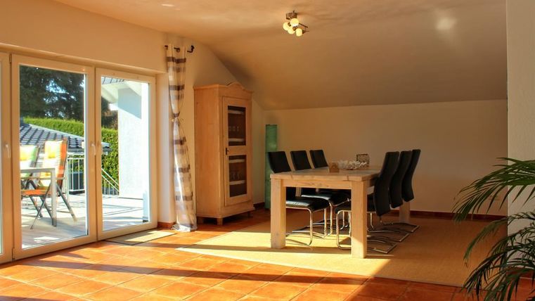 Ein helles Esszimmer mit einem großen Tisch und schwarzen Stühlen. Große Fenster lassen viel Licht herein und bieten einen Blick auf die Terrasse.