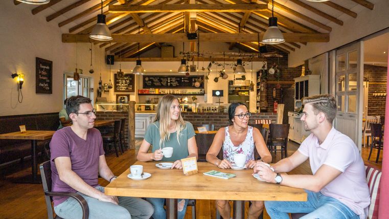 Eine Gruppe von vier Freunden sitzt an einem Holztisch in einem gemütlichen Café. Sie lachen und genießen ihre Getränke in einer einladenden Atmosphäre.