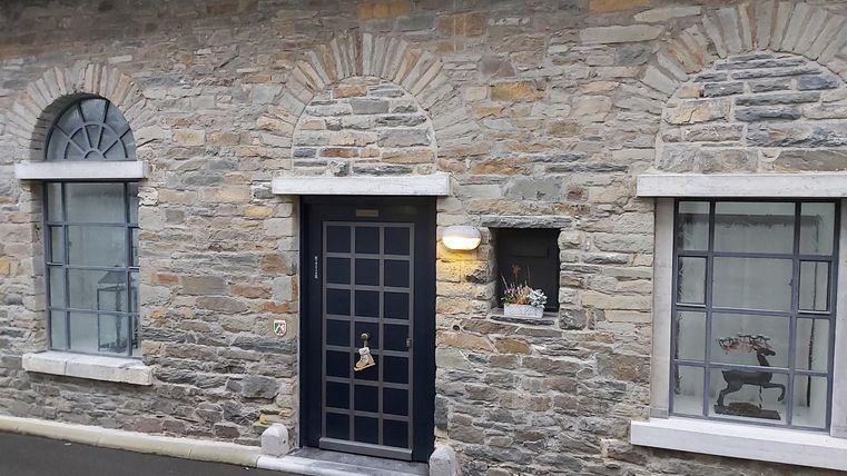 Eine historische Steinmauer mit Fenster und einer schwarzen Tür. Die Fassade wirkt rustikal und einladend.