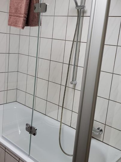 Ein modernes Badezimmer mit einer Badewanne und einer Duschabtrennung aus Glas. Ein pinkes Handtuch hängt an der Wand.