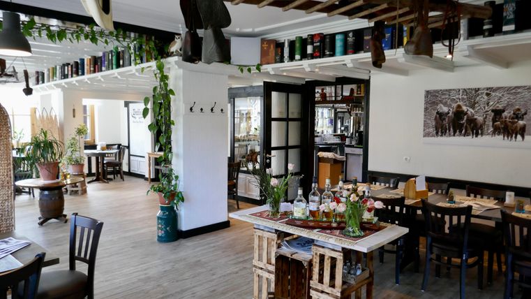 Ein modernes Restaurant mit Holz- und Pflanzenakzenten. Die Einrichtung ist gemütlich und einladend, mit Tischen und dekorativen Elementen.