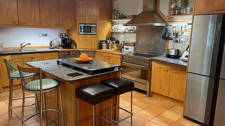 Eine moderne Küche mit Holzschränken und einem großen Kochblock. Auf der Arbeitsfläche liegt eine Orange, und die Geräte sind gut sichtbar.