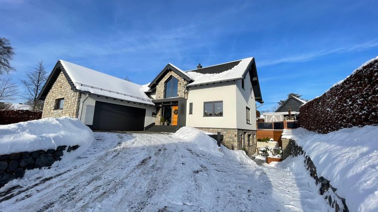 Ein modernes Haus mit einem schneebedeckten Vorgarten. Der Himmel ist klar und blau.
